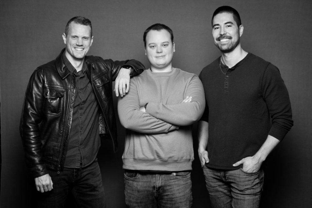 A grayscale photo of three men standing against a neutral background.