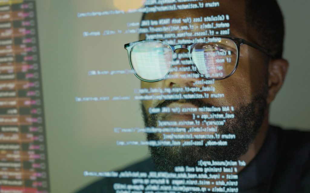 For open-source programs, AI coding tools are a mixed blessing Man studying a see-through display depicting Python computer coding.
