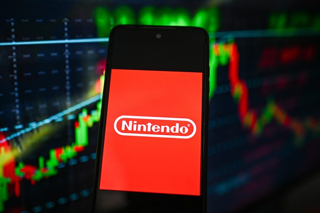 Nintendo logo is seen displayed on a smartphone with stock market percentages on the background.