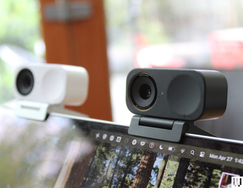 Two small rectangular webcams clipped to the top of a laptop screen one in white and the other black