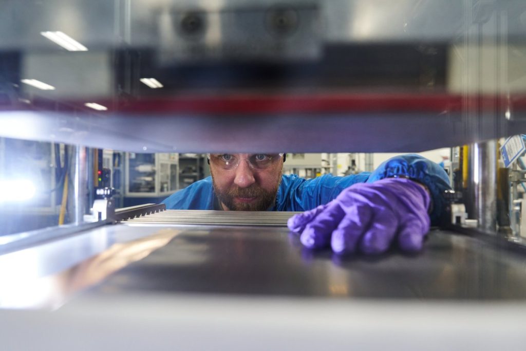 A man reaches his hand into a machine to grab a battery prototype.